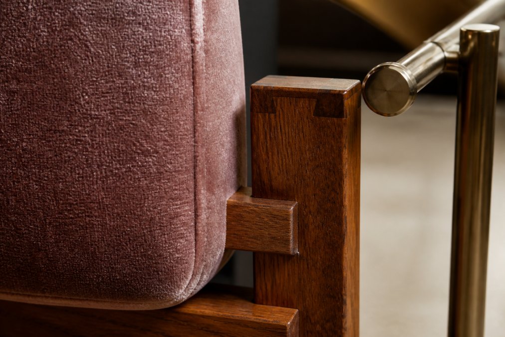 Close-up of premium velvet upholstery texture with visible weave, solid wood frame joinery showing mortise-and-tenon construction, and polished metal hardware detail under warm studio lighting