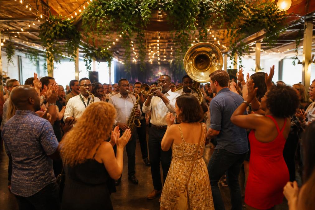 Diverse employees dancing and clapping to a live brass band during a lively event for corporate engagement ideas.