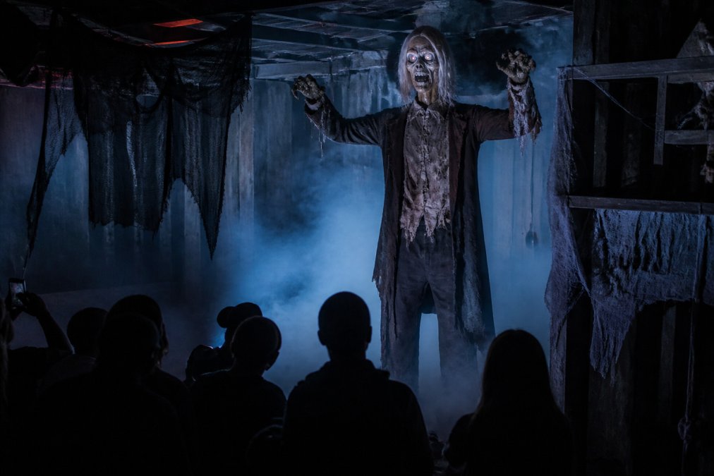 Life-size animatronic horror props stand in a fog-filled room with visitors watching in the dark.