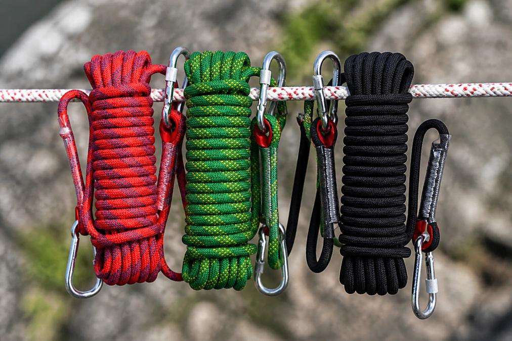 Close-up of various sewn loop climbing slings in different colors and widths arranged on a climbing rope, showing the stitched construction details and webbing texture under natural outdoor lighting