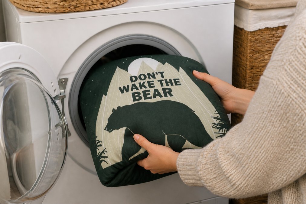 Close-up of hands gently placing a folded blanket into a washing machine, showing careful handling and proper loading technique, warm home laundry room setting