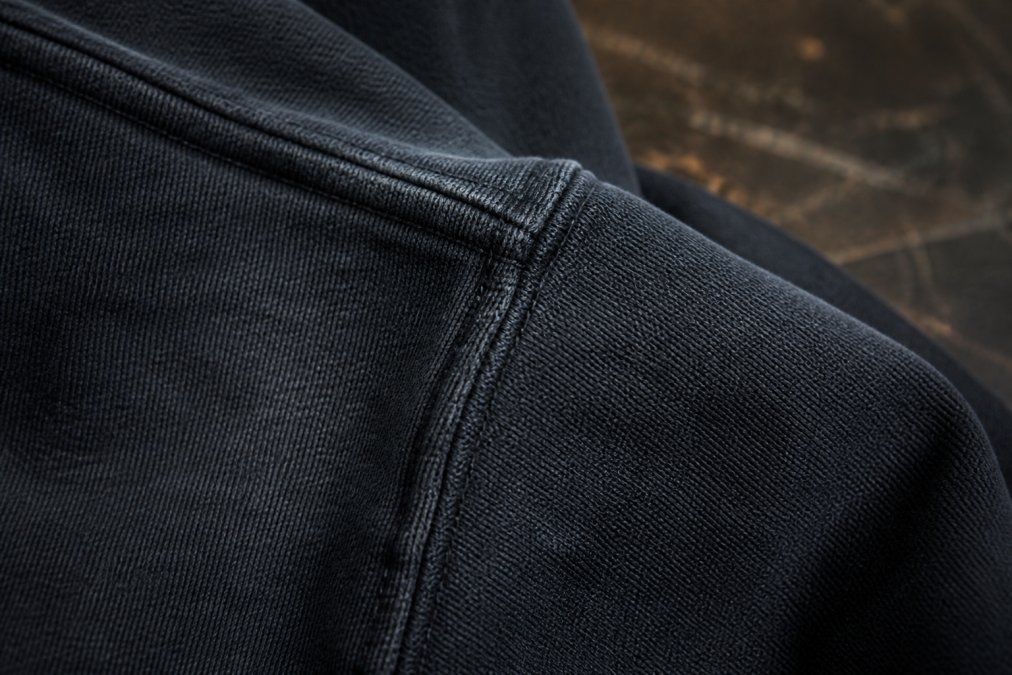 Close-up of heavyweight premium cotton fabric showing tight weave structure and reinforced seam stitching detail under natural light