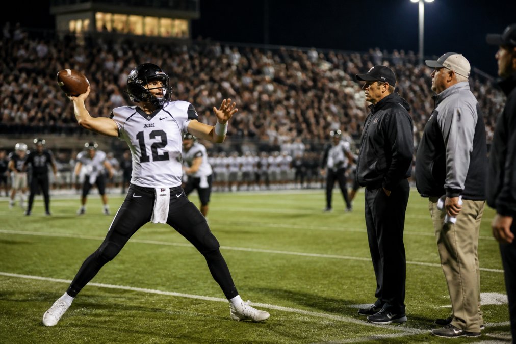 High school quarterback throwing during a game, observed by scouts evaluating football scholarship requirements