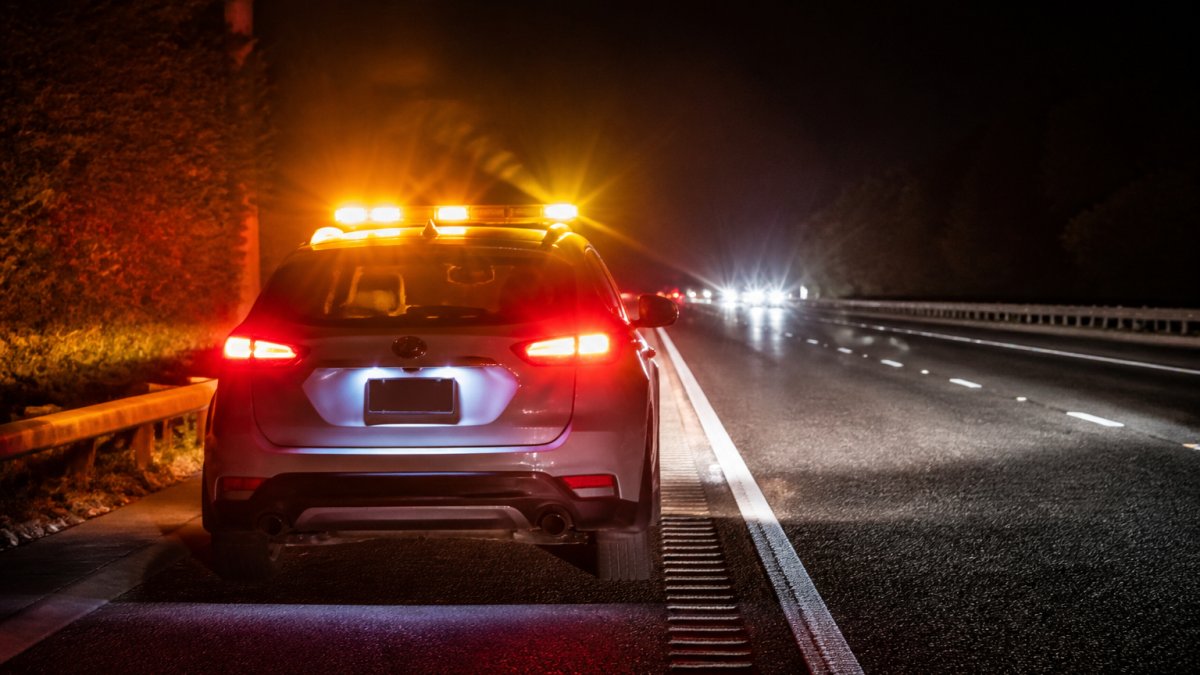 High-visibility lighting and driver behaviour: A practical guide Stationary vehicle on motorway at night with flashing amber and red emergency beacons activated, high-visibility lighting illuminating the vehicle's outline, approaching vehicle headlights visible in the distance on dark asphalt