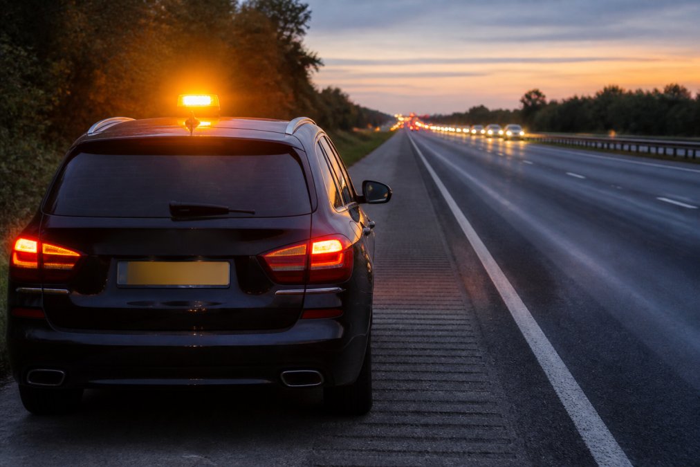 High Visibility Roadside Safety Equipment Guide A stationary vehicle on a motorway hard shoulder at dusk with an amber emergency beacon flashing on the roof, showing 360-degree visibility with warm lighting and approaching traffic visible in the distance