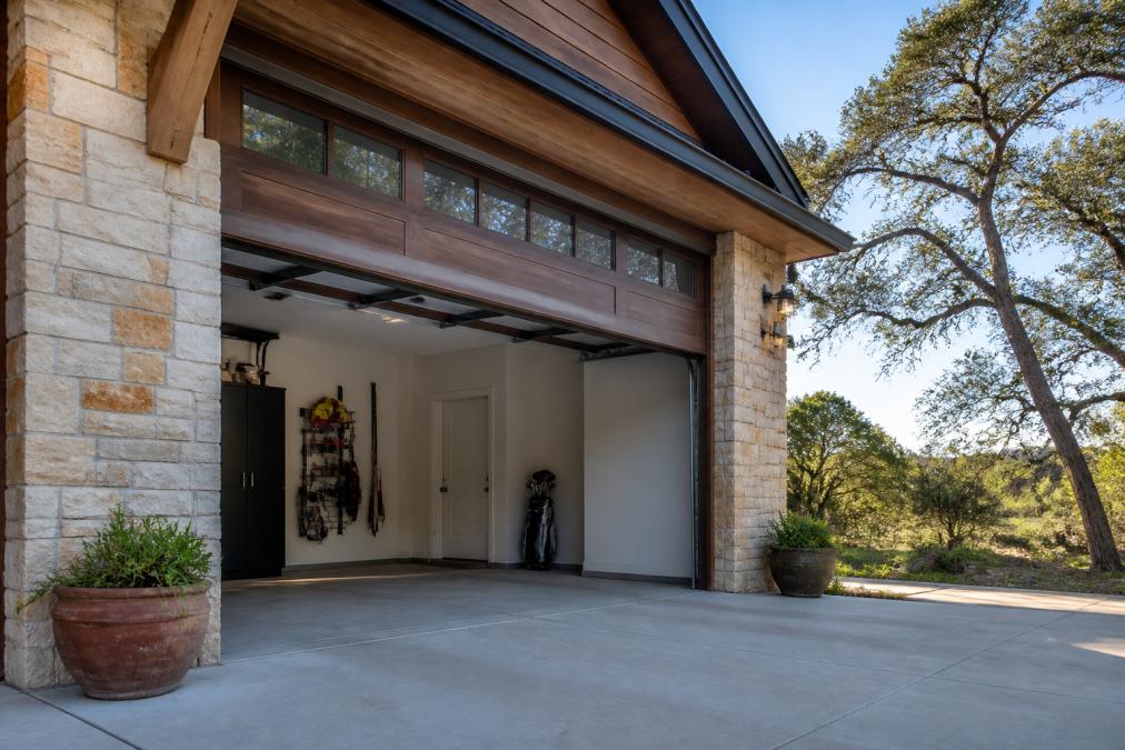 Beautifully installed carriage house style garage door on a modern Texas home with stone and wood exterior, showing the door in open position with trees and natural landscape in background