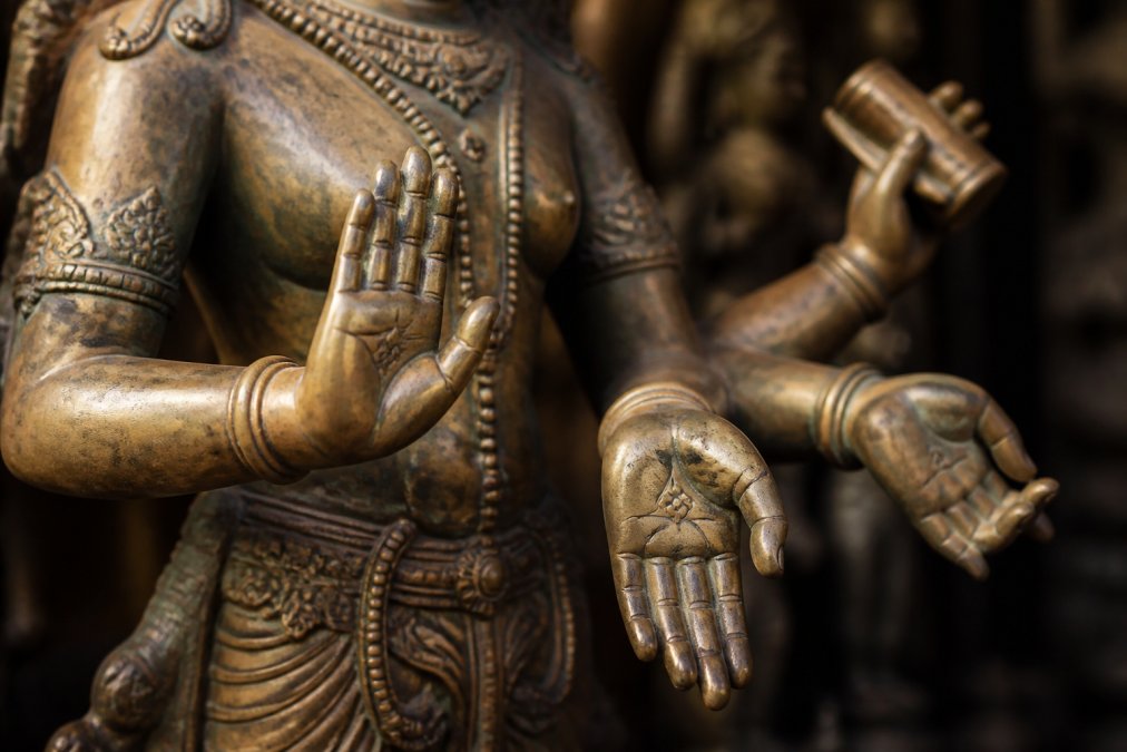 Close-up of ornate bronze Hindu deity statue hands displaying sacred mudras and symbolic hand gestures with intricate finger positioning and divine attributes in temple lighting