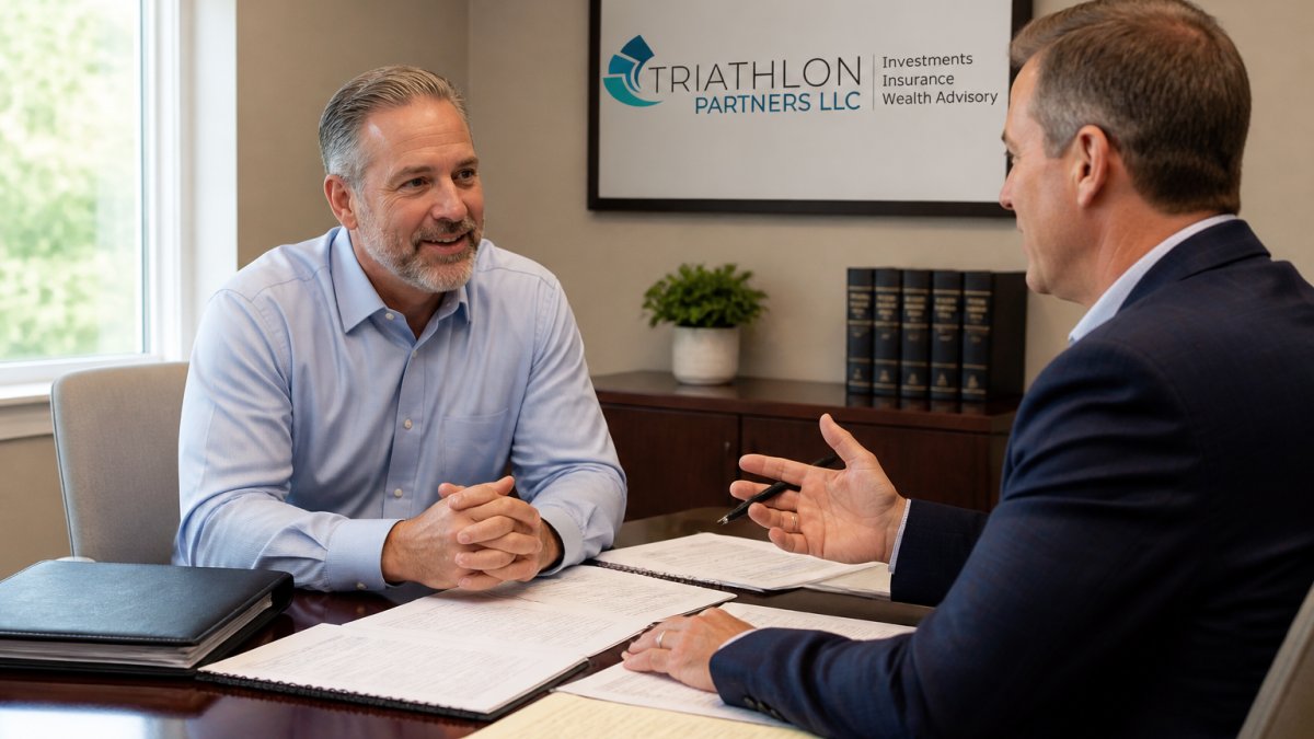 A business owner in his fifties sitting across a desk from a financial advisor in a bright office, documents and a laptop open between them, both engaged in conversation