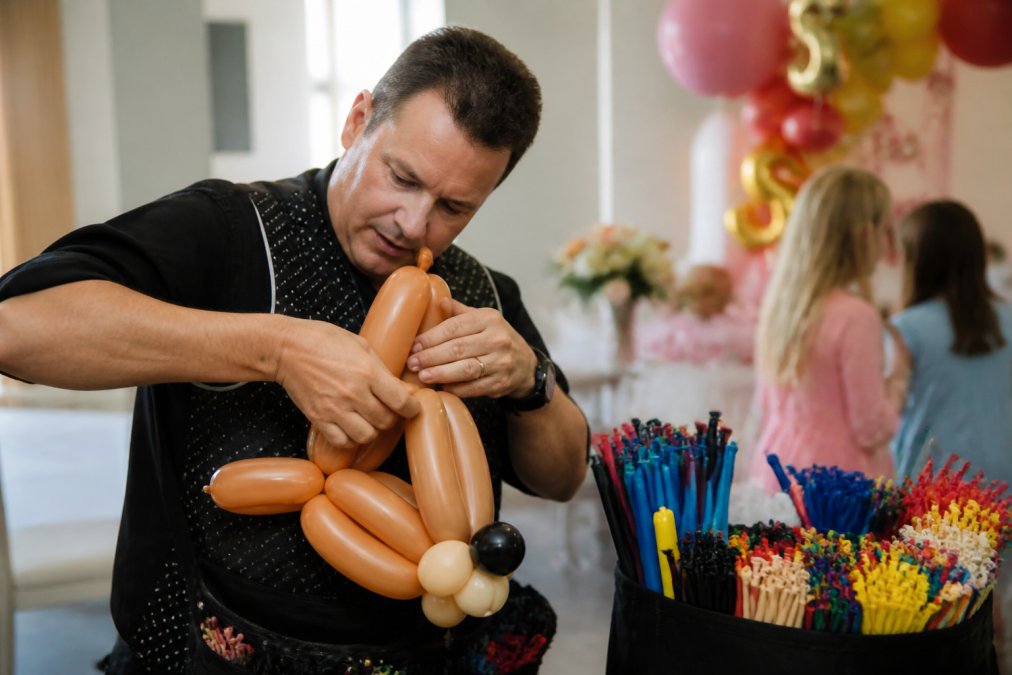 CBA certified balloon artist's hands expertly creating detailed balloon animal sculpture and custom designs at a children's birthday party, precise folding technique visible, focused concentration on intricate details