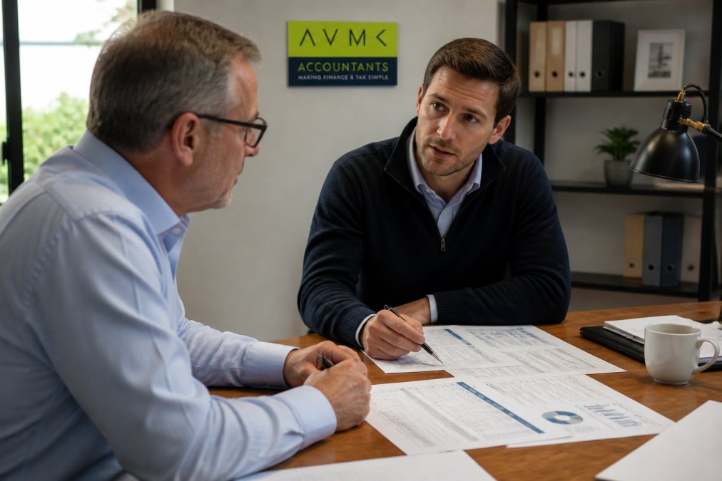 A business owner and a finance professional sitting across a desk reviewing printed financial reports together in a professional office setting, with warm office lighting and papers spread between them