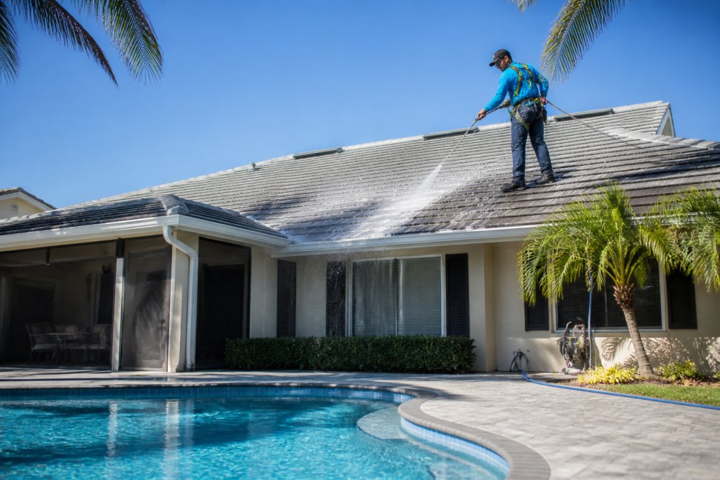 Technician performing insured pressure washing on a Florida shingle roof using a low-pressure soft wash wand