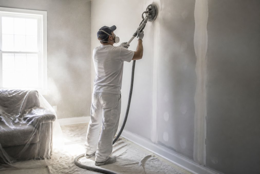 Professional painters sanding a wall seam in a home interior with dust visible in the light.