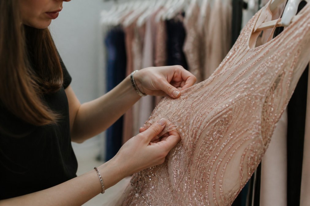 Close-up of woman's hands carefully inspecting formal dress for details, checking fabric quality, seams, and construction with focused attention