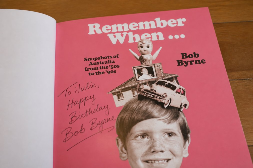 Close-up of an author-signed book cover showing handwritten dedication and vintage Australian photographs, with soft warm lighting highlighting the personalised inscription