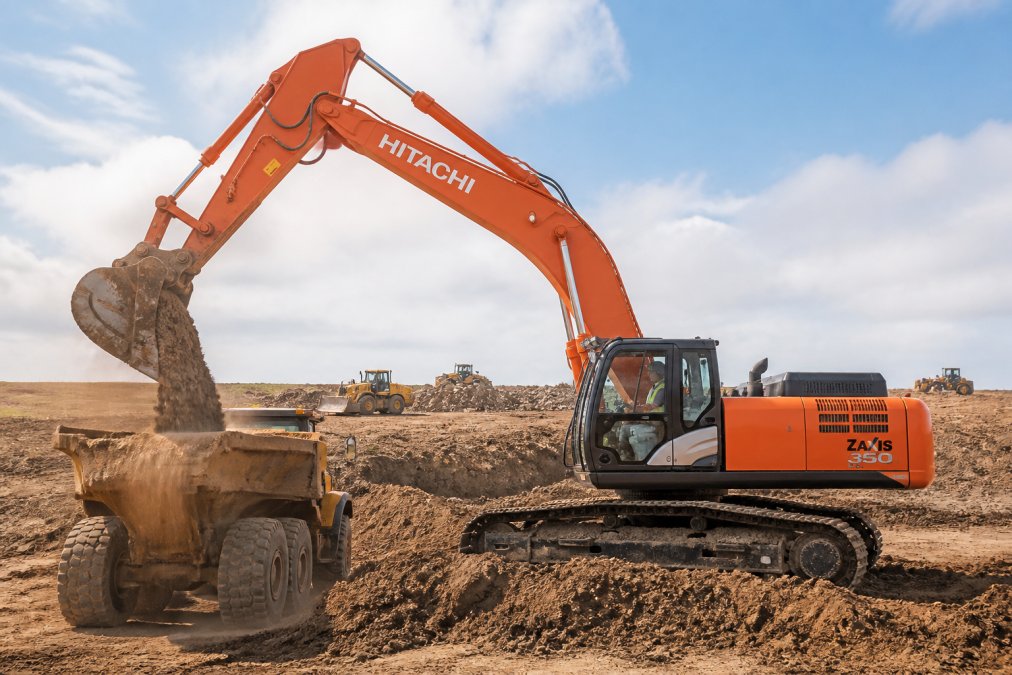 Hitachi construction excavator loading dirt into a dump truck at an active job site during the day