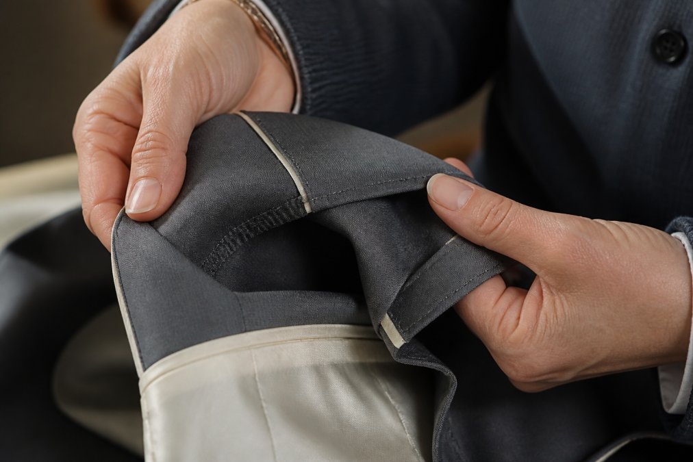 Nahaufnahme der Hände einer Person, die die Innennaht und den Saum einer hochwertigen Jacke untersucht und dabei den Stoff zwischen den Fingern hält, natürliches Licht