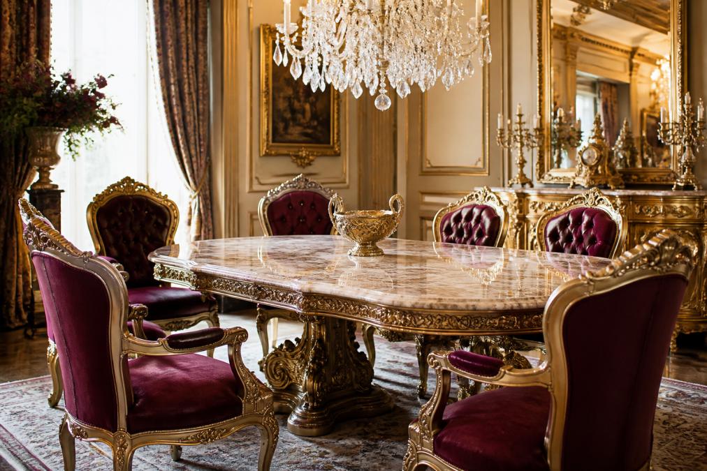 Luxuriöses Esszimmer mit Barock Esstisch aus Marmor, elegantem Kronleuchter und kunstvoll gepolsterten Barock Sesseln in tiefem Samtstoff, goldene Akzente auf Holzschnitzereien