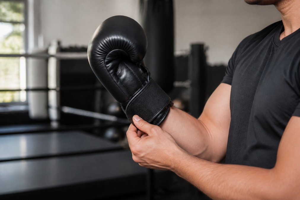 Close-up van een bokser die een zwarte bokshandschoen aantrekt en de klittenbandsluiting strak vastmaakt, hand omhoog zodat de pasvorm bij pols en knokkels zichtbaar is, natuurlijk licht in een sportschool