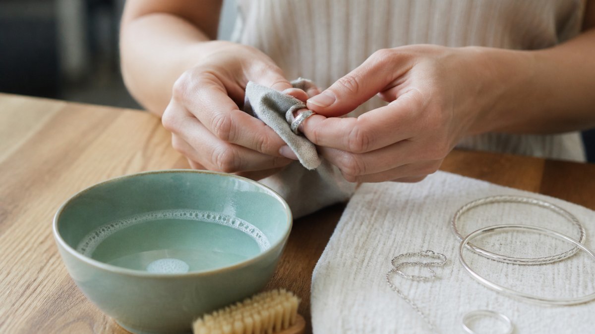 Stappenplan in beeld: handen drogen voorzichtig een zilveren ring af met een zachte doek op een houten tafel.