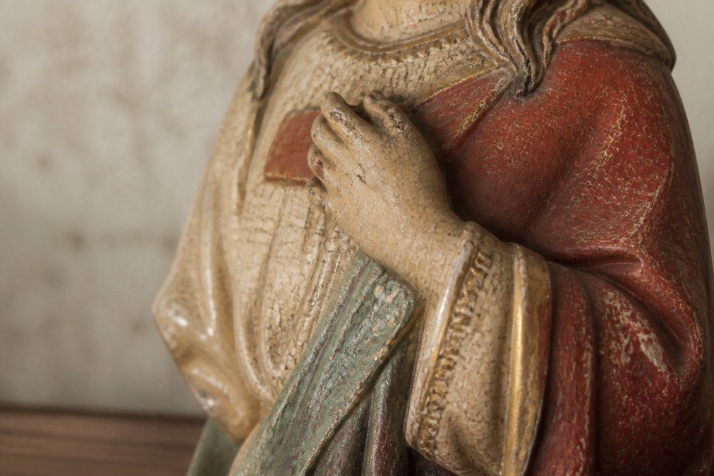 Detailweergave van een antiek gipsen heiligenbeeld met zichtbare krakelures in de polychrome beschildering, waarbij de fijne scheurtjes en versleten kleurlagen de authenticiteit en leeftijd demonstreren