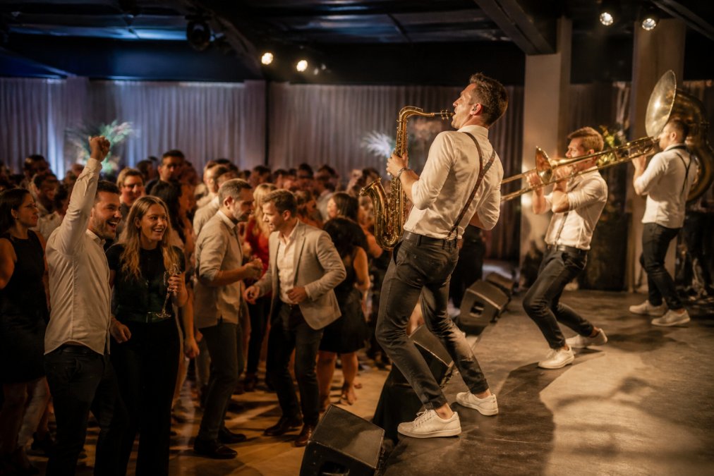 Professionele liveband optredend op zakelijk evenement met dansende gasten, energieke sfeer, muzikanten in beweging op podium met warm licht