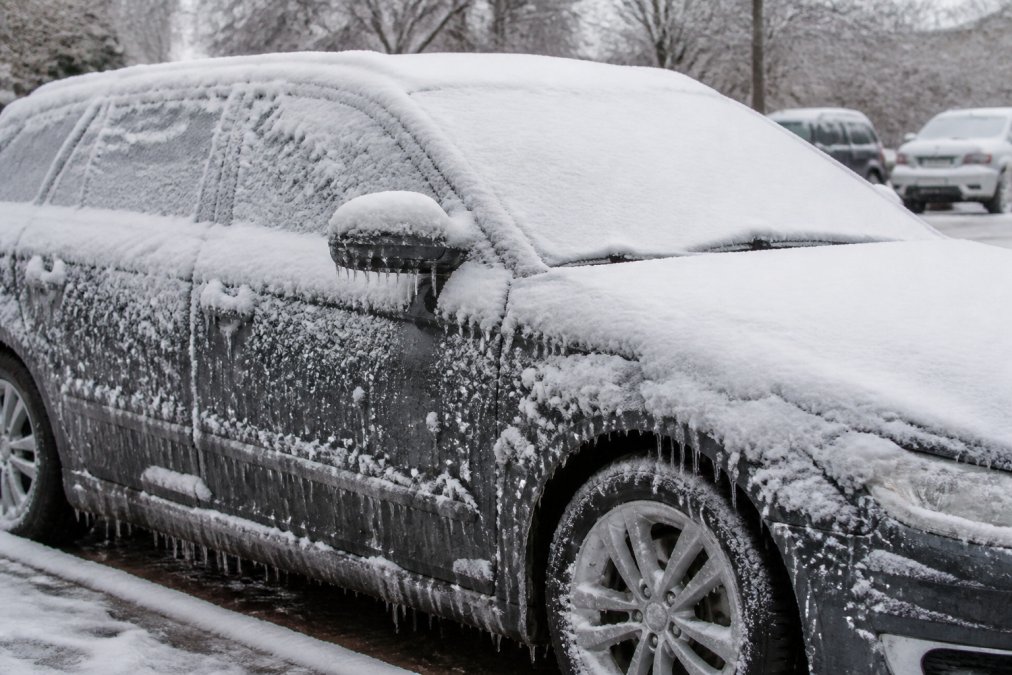 Winterse auto bedekt met sneeuw en ijsvorming op het dak en zijkanten, toont de rauwe weersomstandigheden en de noodzaak van lakbescherming tegen pekel en vorst