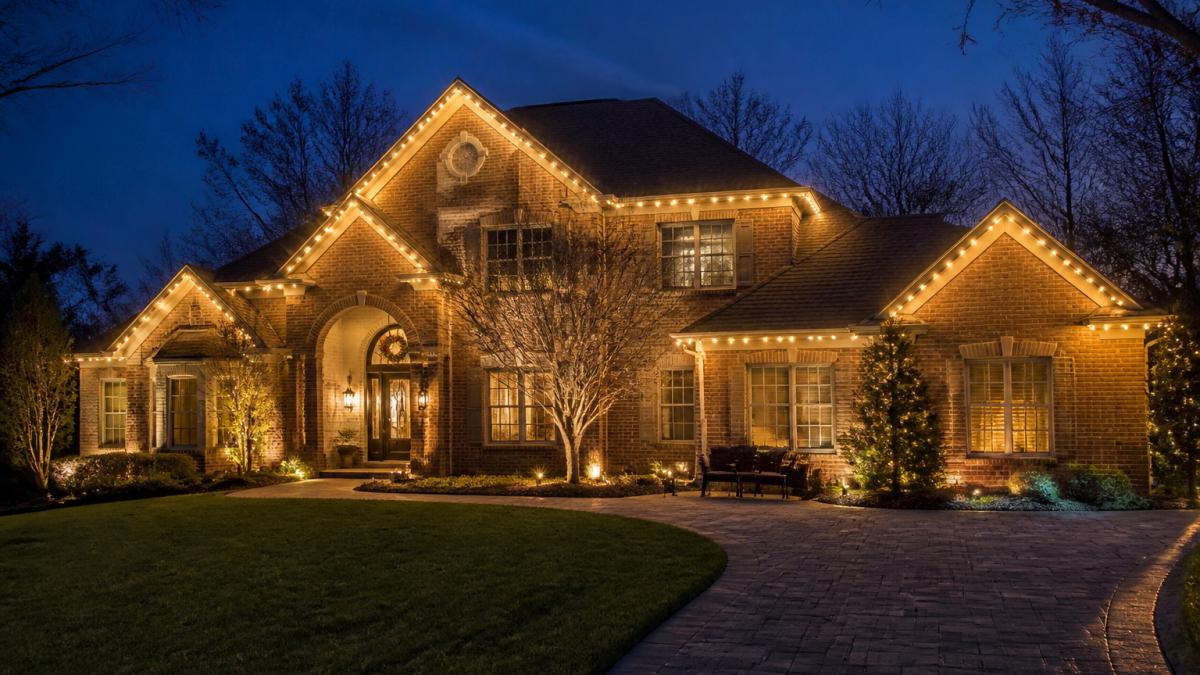 Elegant home at dusk featuring warm white holiday lighting and décor outlining the roofline and architecture.