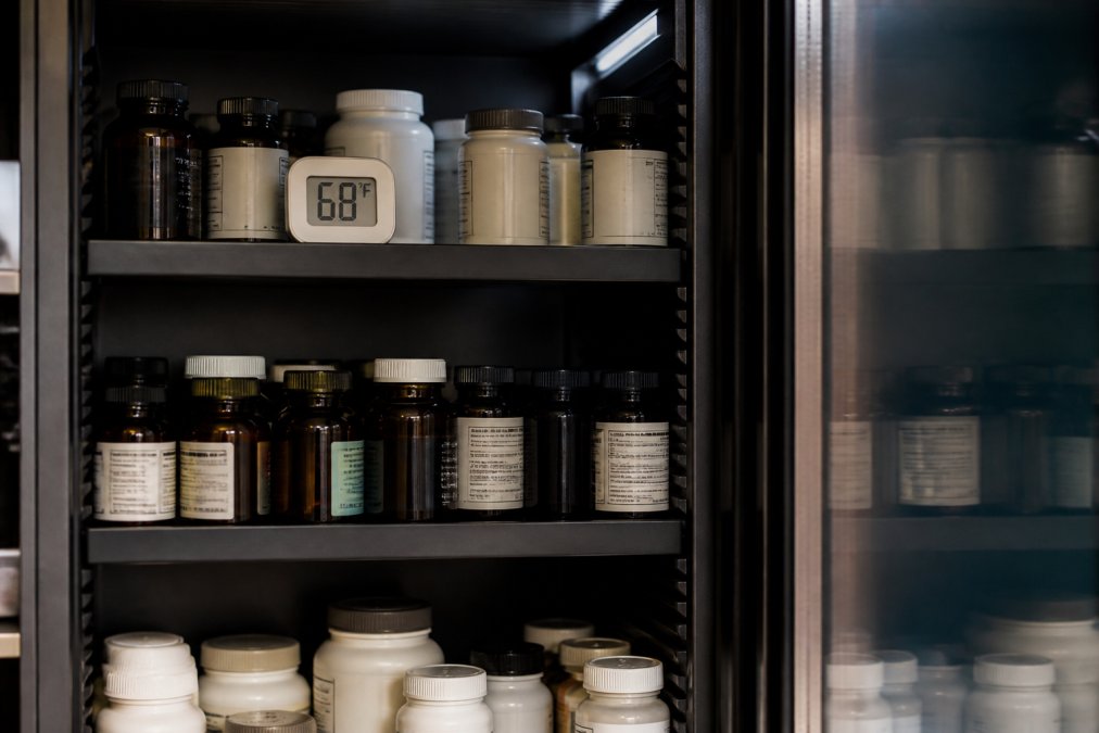 Organized supplement bottles stored on shelves in a climate-controlled cabinet with a digital thermometer displaying 68°F, showing proper storage environment with minimal light exposure