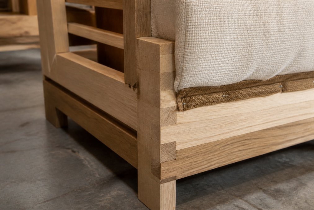 Close-up of solid wood frame joinery showing dovetail construction and kiln-dried hardwood details on upholstered furniture, with natural workshop lighting highlighting the frame quality and craftsmanship