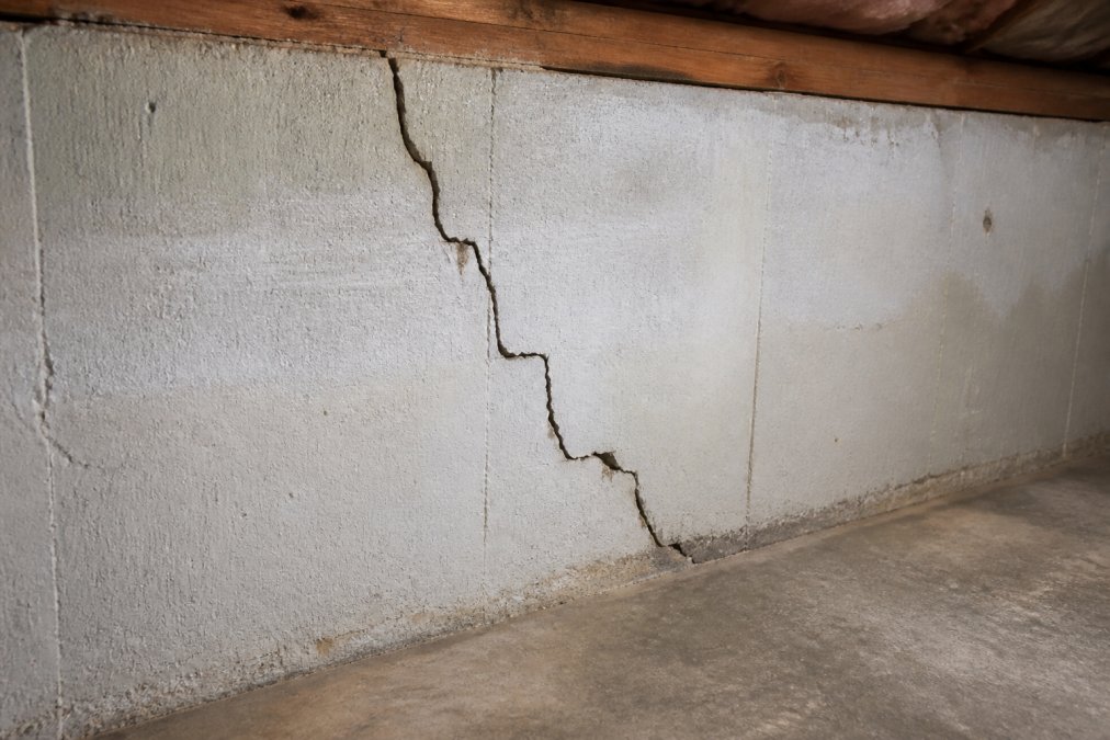Close-up of a visible structural crack in a residential foundation wall, with natural lighting showing the extent of the damage in a basement setting