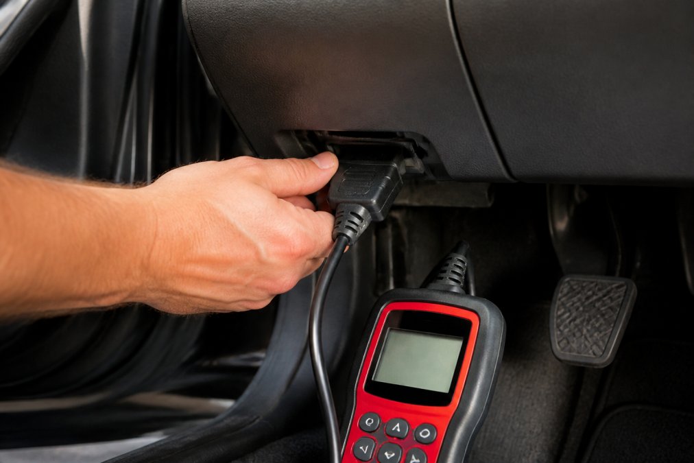 Hand plugging an OBD-II scanner into a dashboard port to diagnose a Honda check engine light in a home garage.
