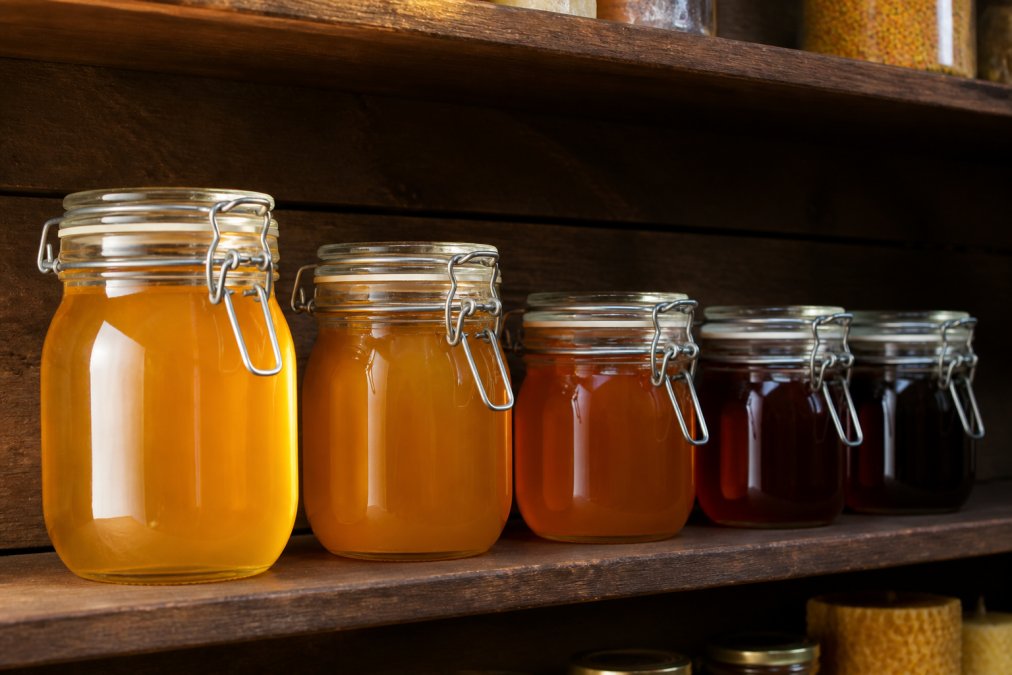 Mehrere luftdichte Gläser mit hellem und dunklem Honig auf einem dunklen Holzregal, um Honig richtig lagern zu können.