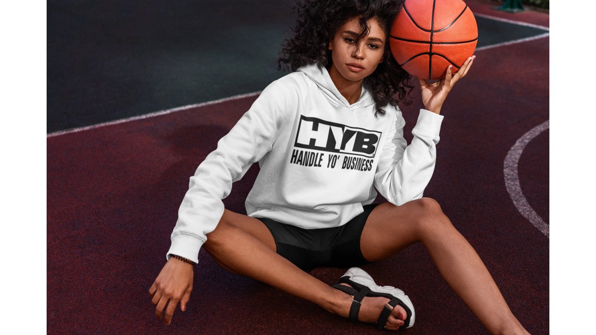 A confident person wearing a dark graphic hoodie paired with clean dark joggers and fresh white sneakers, standing in a modern co-working space with exposed brick walls and warm ambient lighting, projecting a polished streetwear-meets-business look