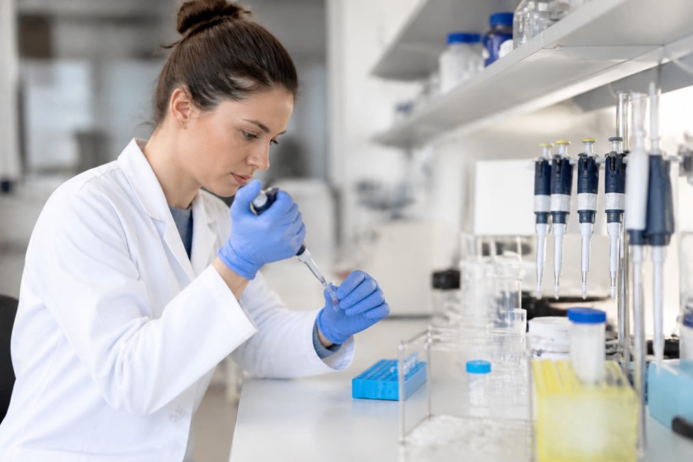 Onderzoeker in laboratoriumjas die voorzichtig een peptide-monster voorbereidt in een schone werkplek met pipetten en reageerbuisjes, professionele verlichting in modern onderzoekslaboratorium