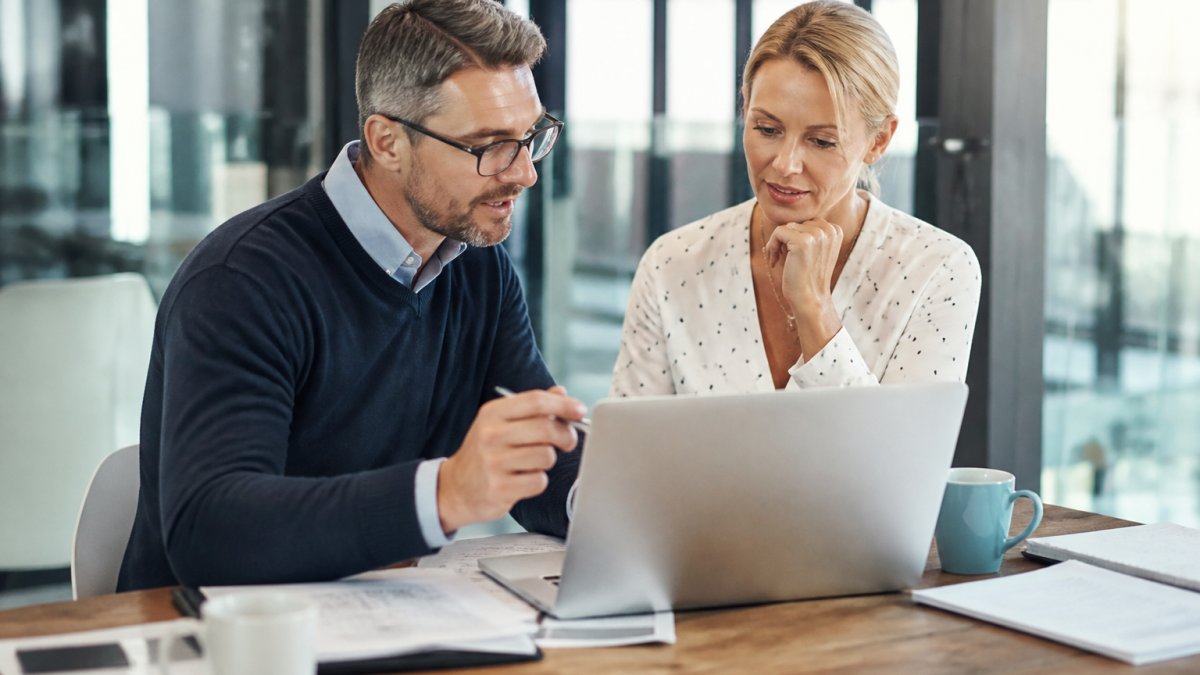 A consultant and a small business owner reviewing a workflow diagram on a laptop in a bright office, with printed process notes and coffee on the table