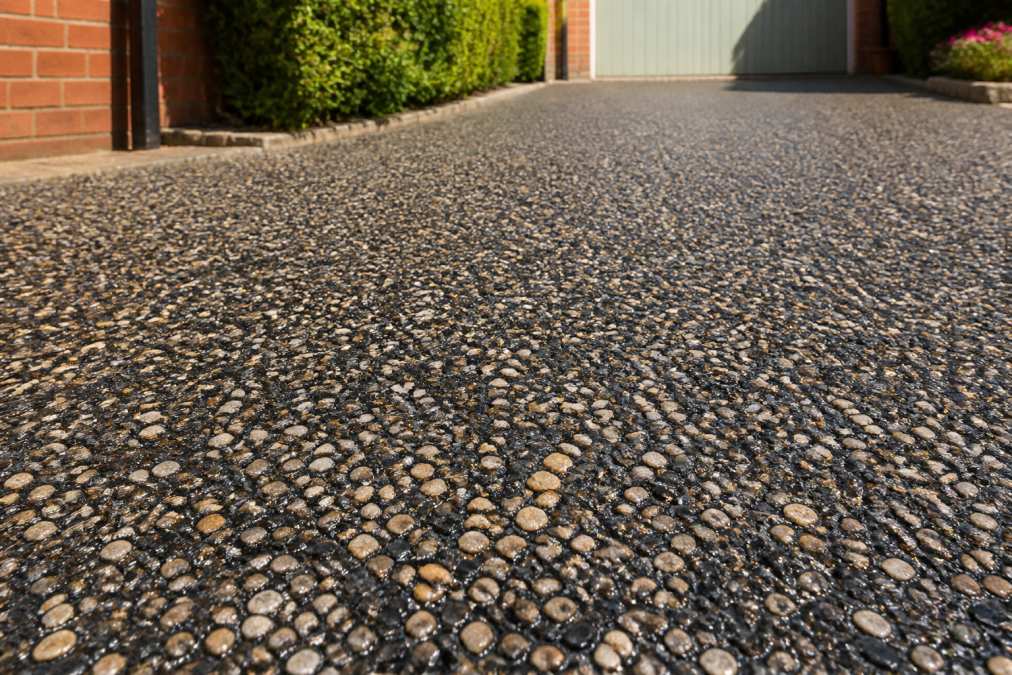 Close-up of newly installed hot tar and chip driveway surface with visible stone chips embedded in dark asphalt, showing natural rustic texture under bright daylight