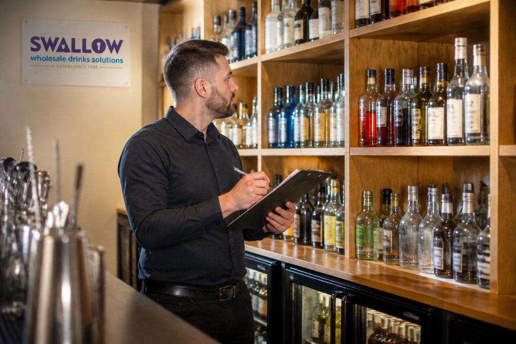 Bar manager checking premium inventory on shelves to support drink cost control efforts in a modern hotel bar