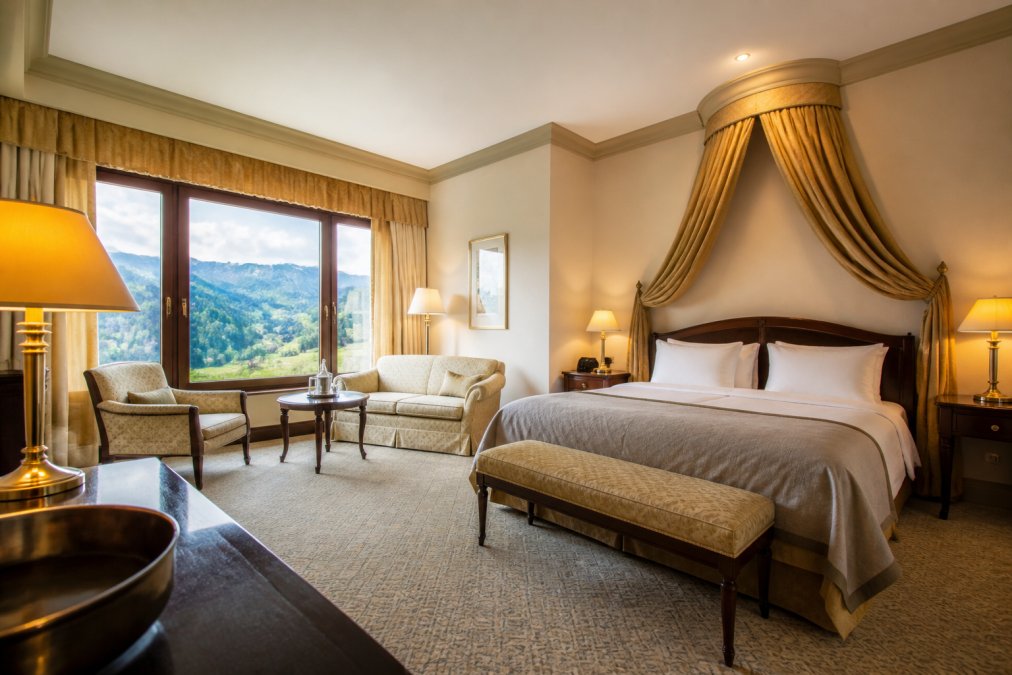 Elegantes Hotelzimmer mit klassischen Möbeln, großem Fenster zum Alpenpanorama, luxuriösen Textilien, warmer Beleuchtung und modernem Badezimmer