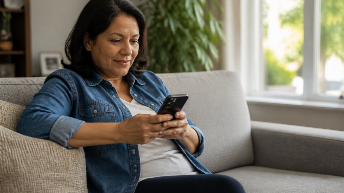 Patient sitting on home couch using smartphone to search for healthcare information, warm natural lighting through window, relaxed home environment