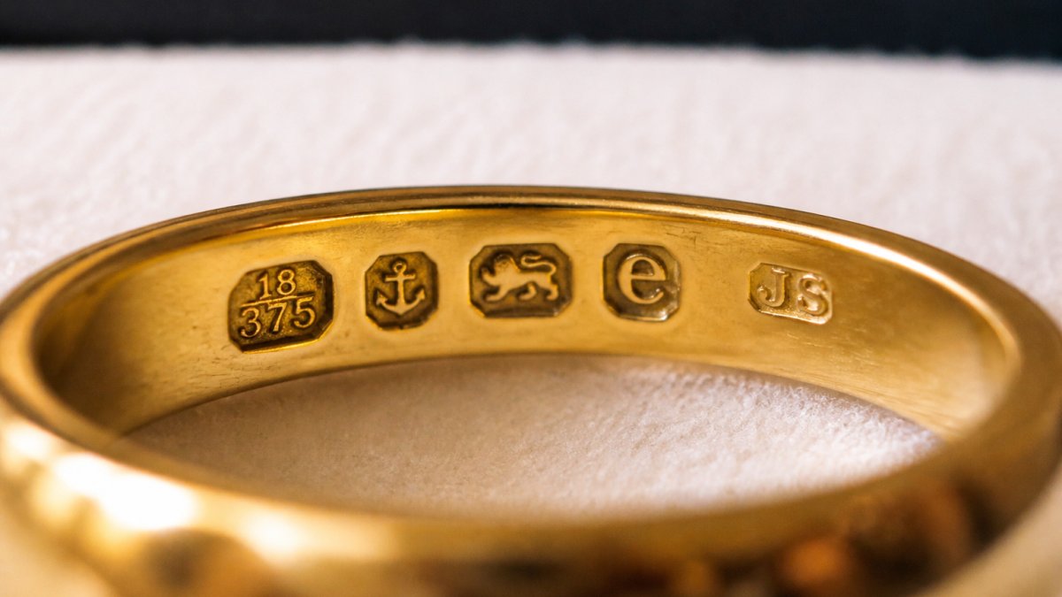 Close-up of antique gold ring showing stamped hallmarks and maker's marks under bright light, with details of the metal surface clearly visible