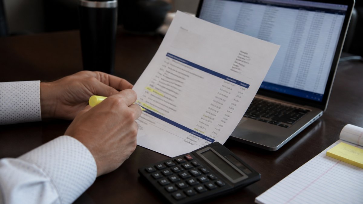 Steps for a dealership software cost audit shown through an invoice review with a calculator and spreadsheet.