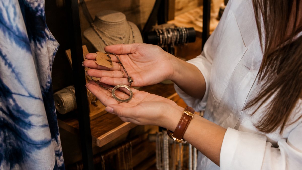 Woman’s hands holding a handcrafted artisan necklace as a unique gift in a cozy, sunlit boutique setting.