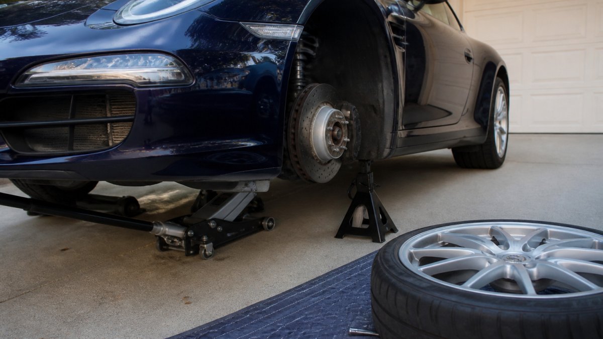 Mechanic using a floor jack and jack stands to lift a car for wheel removal on a paved driveway