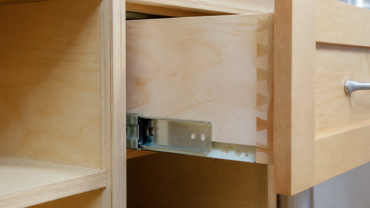 Close-up of cabinet interior showing solid plywood box construction with dovetail drawer joinery and visible wood grain, soft-close hardware installed on drawer slide