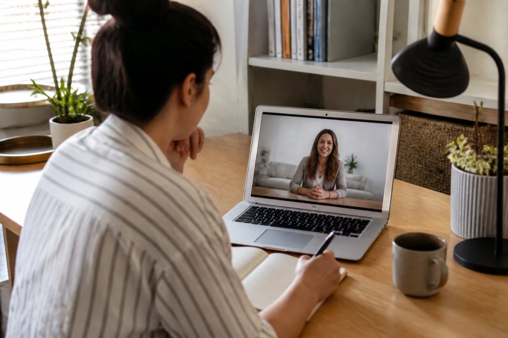 Person sitting comfortably at a home desk using telehealth for anxiety on a laptop with a notebook nearby.