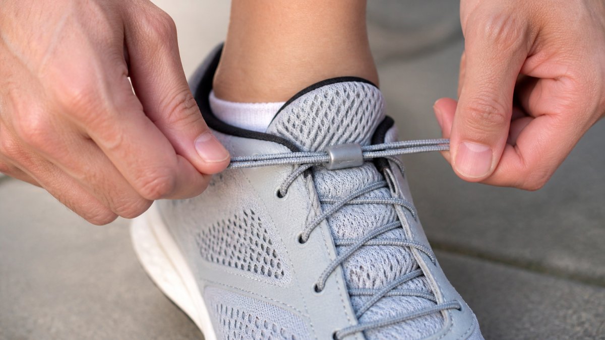 Close-up of a person's hands adjusting elastic laces on a running shoe, showing the stretch and flex of the laces against the shoe tongue, with a relaxed foot in the shoe