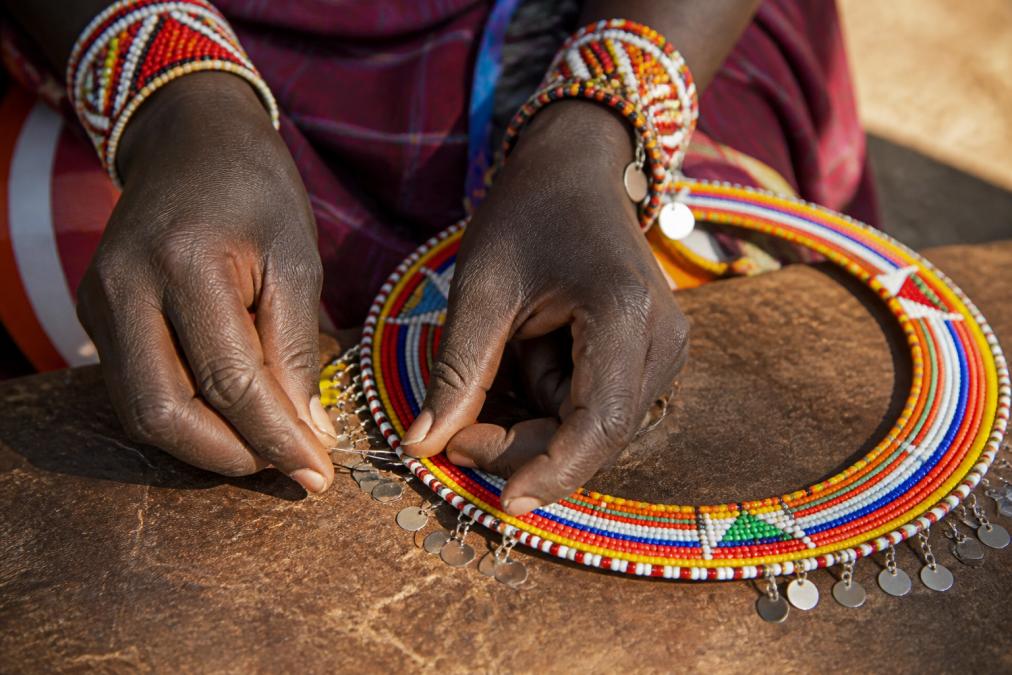 Close-up of artisan hands working intricate beadwork on traditional East African jewelry, fingers carefully placing each bead with precision, natural sunlight illuminating the detailed craftsmanship