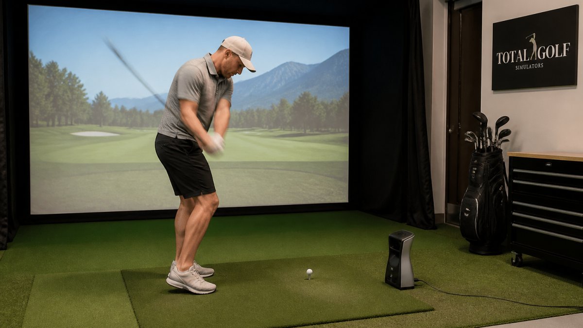 Golfer swinging a club in a simulator bay with a launch monitor on the mat