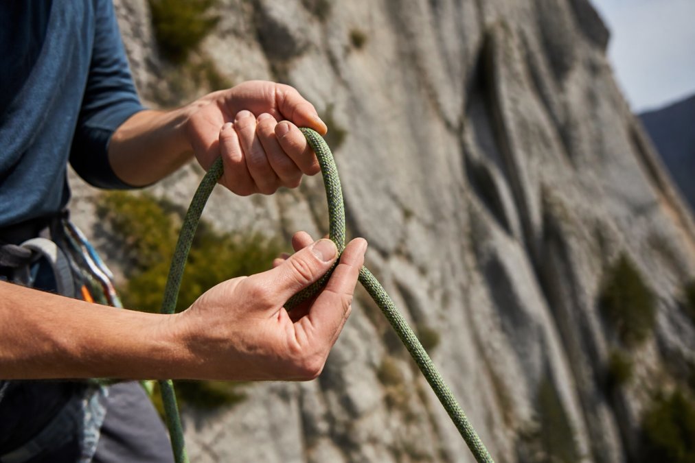 Climber running hands along climbing ropes to inspect for sheath damage at a rocky crag