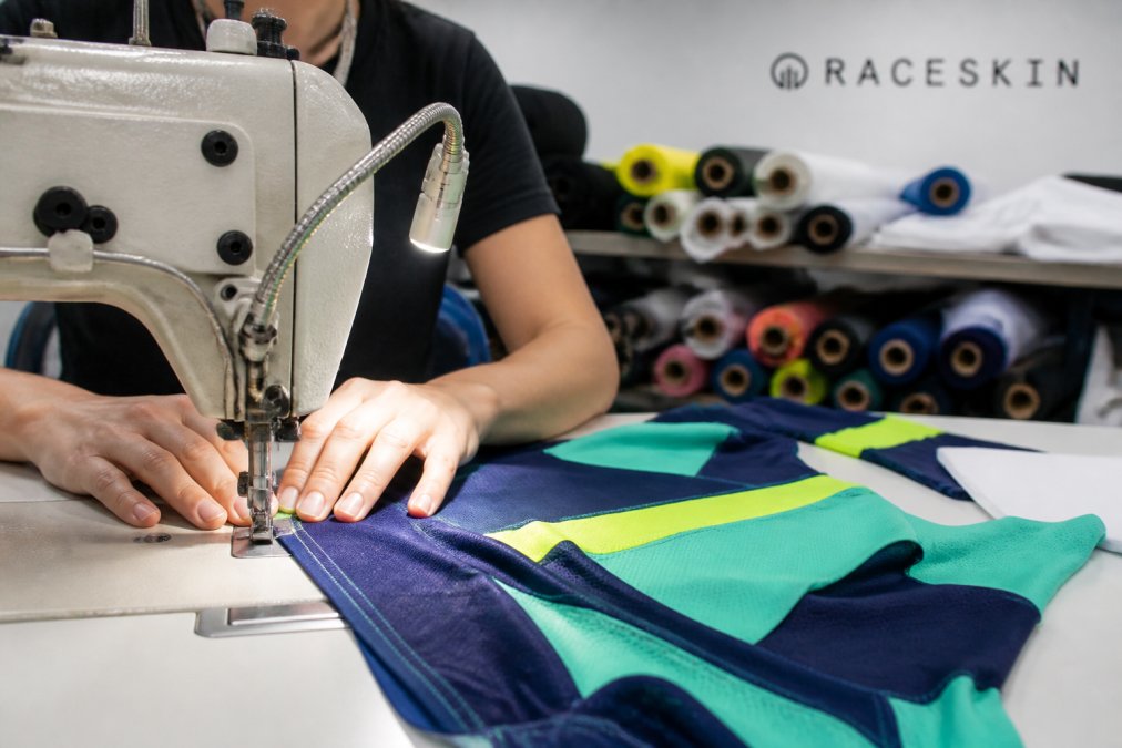 Sewing machine stitching a colorful jersey for custom kits in a bright textile workshop with fabric rolls